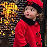 Kayan is registered to the contest to win money with this photo: toddler, child, red_coat, hat, roses, fireplace, fire, mesh_screen, outdoor, winter_clothing, curious, portrait, warm, glowing, face, person, standing, looking_away, cute, seasonal