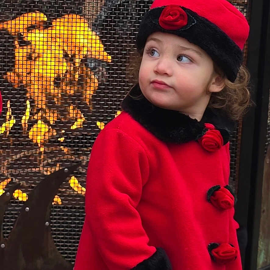 Kayan is registered to the contest to win money with this photo: child, curious, cute, face, fire, fireplace, glowing, hat, looking_away, mesh_screen, outdoor, person, portrait, red_coat, roses, seasonal, standing, toddler, warm, winter_clothing