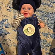 Michael is registered to the contest to win money with this photo: baby, infant, 6_months, smiling, blue_outfit, striped_shirt, hat, pom_poms, lying_down, carpet, indoor, cute, happy, child, person, small_hands, blue, beige, patterned_rug, playful