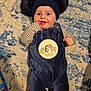 baby, infant, 6_months, smiling, blue_outfit, striped_shirt, hat, pom_poms, lying_down, carpet, indoor, cute, happy, child, person, small_hands, blue, beige, patterned_rug, playful