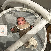 Amaury participe au concours pour gagner de l'argent avec cette photo : baby, infant, play_mat, clothing, bib, face, person, indoor, toy, play_gym, milestone_card, floor, socks, woolen_sweater, cute, lying_down, soft_texture, grey, white, decorative