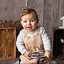 child, baby, toddler, one_year, first_birthday, smiling, portrait, indoor, wooden_background, crate, steering_wheel, knit_overall, long_sleeve, sitting, props, cotton_branch, vase, number_one, neutral_colors, studio_photo