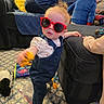 toddler, child, sunglasses, denim_overalls, toy, carpet, sofa, adult, indoor, family, playful, person, furniture, blue_clothing, patterned_rug, living_room, footwearless, red_sunglasses, cute, home