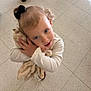 toddler, child, plush_toy, hugging, indoor, floor, tiles, black_hair_bow, cute, affection, looking_up, soft_toy, young_child, casual_clothing, portrait, happy, person, small_hands, curly_hair, innocent