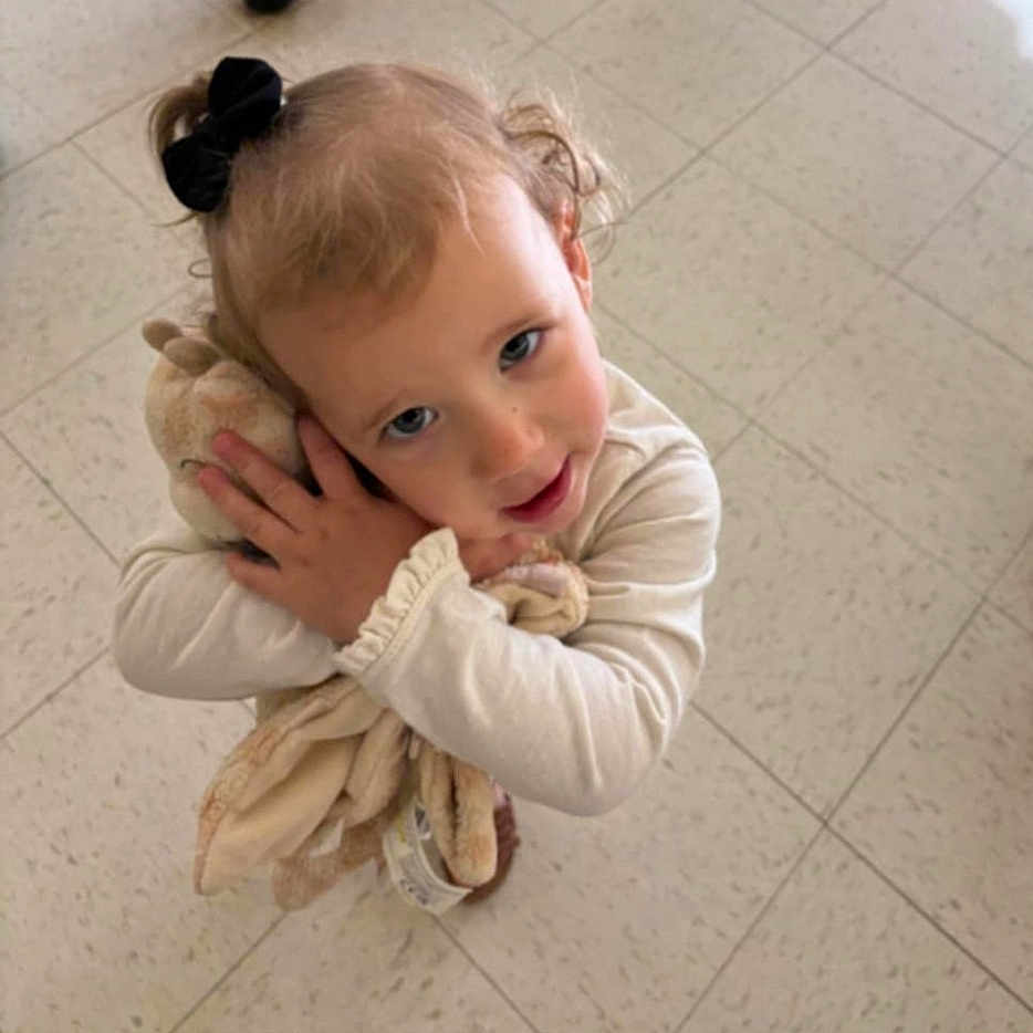 Ryleigh joined the competition — help win amazing prizes! affection, black_hair_bow, casual_clothing, child, curly_hair, cute, floor, happy, hugging, indoor, innocent, looking_up, person, plush_toy, portrait, small_hands, soft_toy, tiles, toddler, young_child