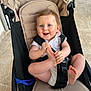 baby, child, stroller, seatbelt, foot, hands, smiling, happy, indoor, floor, tile, clothing, white_shirt, hair, face, blue_eyes, infant, cute, person, sitting