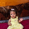 Jazlynn is registered to the contest to win money with this photo: baby, infant, child, portrait, yellow_dress, pink_bow, bed, pillow, blanket, indoors, sitting, lying_down, wide_eyes, curly_hair, smiling, clothing, furniture, bedroom, colorful, photography