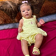 Jazlynn joined the competition — help win amazing prizes! baby, infant, child, portrait, lying_down, bed, bedspread, pillow, dress, yellow_clothing, sandals, hair_bow, sitting, curious, face, hands, legs, indoor, colorful, fashion