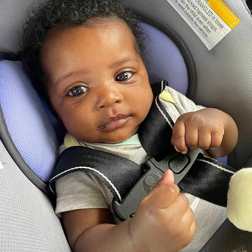Kahlani joined the competition — help win amazing prizes! baby, car_seat, child, infant, seatbelt, straps, face, curly_hair, clothing, looking, young_child, safety, car_interior, person, portrait, cute, hands, expression, seat, indoor