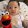 Kylieannah is registered to the contest to win money with this photo: baby, blanket, bow, child, couch, elmo, eyes, face, floral_bedding, hair, indoors, infant, pajamas, pink_clothing, plush_toy, portrait, sitting, smiling, teddy_bear, tongue_out
