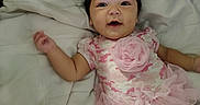 Kylieannah is registered to the contest to win money with this photo: adorable, baby, bed, bedding, camouflage_pattern, child, close_up, dark_hair, flower, indoor, infant, lying_down, open_mouth, photography, pink_outfit, portrait, ruffles, smiling, white_blanket, wide_eyes