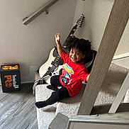 Iziah is registered to the contest to win money with this photo: black_pants, carpet, child, electric_guitar, footwear, guitar, hair, happy, indoors, person, red_shirt, shoebox, smiling, spiderman, stairs, timberland, toddler, wall, waving, wood_floor