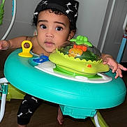 Blaze is registered to the contest to win money with this photo: baby, infant, toddler, child, walker, activity_center, toy, hat, big_eyes, curly_hair, surprised_expression, barefoot, wooden_floor, door, door_handle, indoor, playtime, bright_colors, hand, face