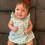 baby, child, smiling, red_bow, dress, cherry_pattern, sitting, couch, indoor, cute, happy, infant, person, portrait, young_child, clothing, furniture, skin, head, face