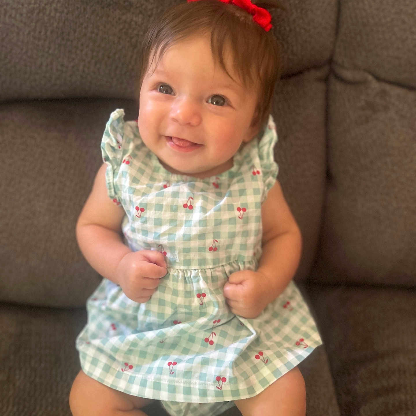Katalia is registered to the contest to win money with this photo: baby, cherry_pattern, child, clothing, couch, cute, dress, face, furniture, happy, head, indoor, infant, person, portrait, red_bow, sitting, skin, smiling, young_child