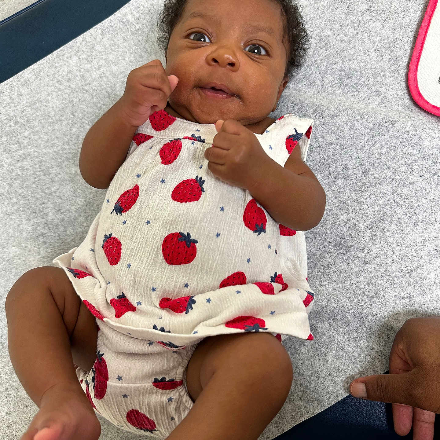Araya joined the competition — help win amazing prizes! baby, child, curly_hair, cute, fist, gray_background, hand, happy, human, indoors, infant, lying_down, one_person, playful, portrait, skin, soft_surface, strawberry_pattern, white_clothing, wide_eyes