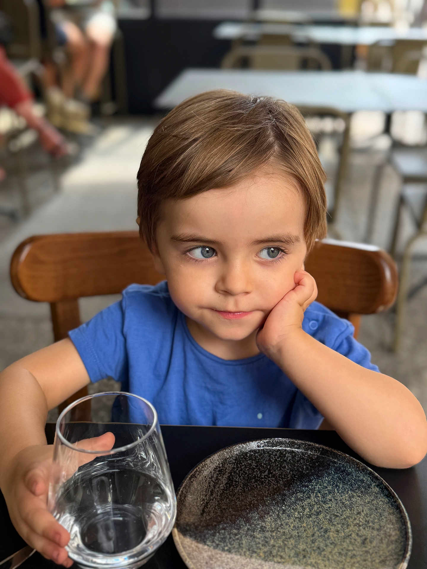 Hugo a rejoint le concours — aidez-le/la à gagner de superbes lots ! child, blue_shirt, glass, water, table, plate, chair, face, person, indoor, curious, young, short_hair, skin, hand, seated, restaurant, reflective, expression, daylight