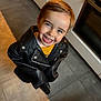 child, smiling, leather_jacket, happy, indoor, kitchen, tile_floor, person, cute, portrait, young_child, fashion, casual, hair, face, standing, joyful, playful, clothing, expression