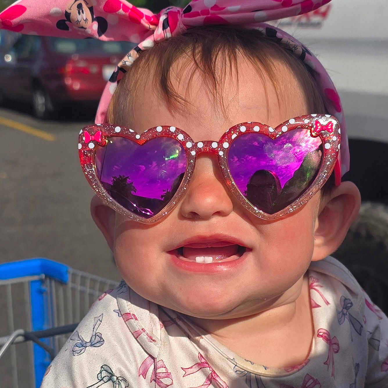 Ellamae is registered to the contest to win money with this photo: toddler, child, sunglasses, heart_shaped, purple_lenses, headband, minnie_mouse, pink, shopping_cart, outdoor, sunlight, smile, teeth, clothing, pattern, bows, cute, happy, portrait, baby