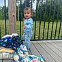 toddler, child, outdoor, deck, wood, blanket, bag, railing, greenery, trees, grass, clothing, jeans, shirt, footwear, expression, standing, person, daylight, nature