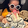 baby, bottle, milk, sunglasses, car_seat, blanket, toy, wooden_sign, 4_months, clothing, infant, cute, child, feeding, accessory, seatbelt, soft_toys, portrait, indoor, headwear