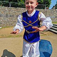 Lorenzo participe au concours pour gagner de l'argent avec cette photo : child, boy, costume, blue, white, playground, outdoor, smiling, happy, tree, stone_wall, daylight, shadow, steps, belt, fabric, person, playing, fun, park