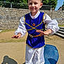 child, boy, costume, blue, white, playground, outdoor, smiling, happy, tree, stone_wall, daylight, shadow, steps, belt, fabric, person, playing, fun, park