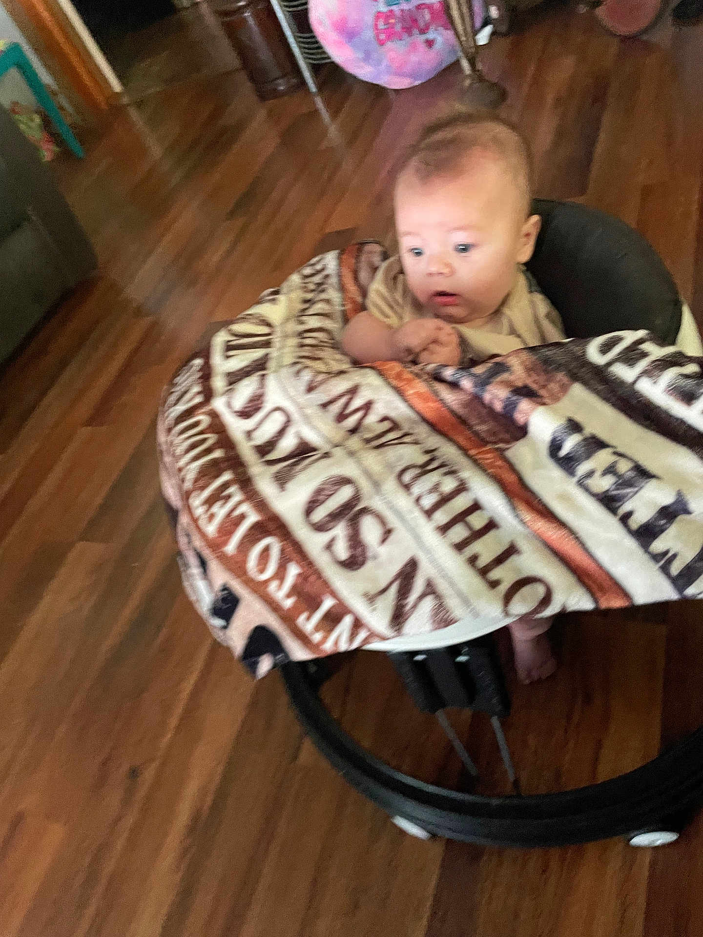 Levi is registered to the contest to win money with this photo: baby, blanket, baby_rocker, wooden_floor, indoor, curious, child, infant, person, furniture, home, flooring, seat, expression, clothing, young, portrait, cozy, wrapped, looking