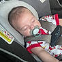 Levi is registered to the contest to win money with this photo: baby, sleeping, car_seat, pacifier, child, infant, seatbelt, safety, clothing, cute, resting, indoors, warning_label, closeup, portrait, toddler, baby_outfit, peaceful, head, arm