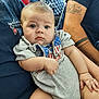 baby, infant, person, child, blue_eyes, onesie, american_flag, arm, tattoo, casual_clothing, indoor, seated, curious_expression, chubby, holding, adult, background, blurred, skin, closeup