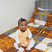 Fatima joined the competition — help win amazing prizes! baby, child, smiling, sitting, bed, bedspread, plaid_pattern, floral_pattern, rose, indoors, cute, happy, person, clothing, white_socks, long_sleeves, head, hair, tongue_out, room