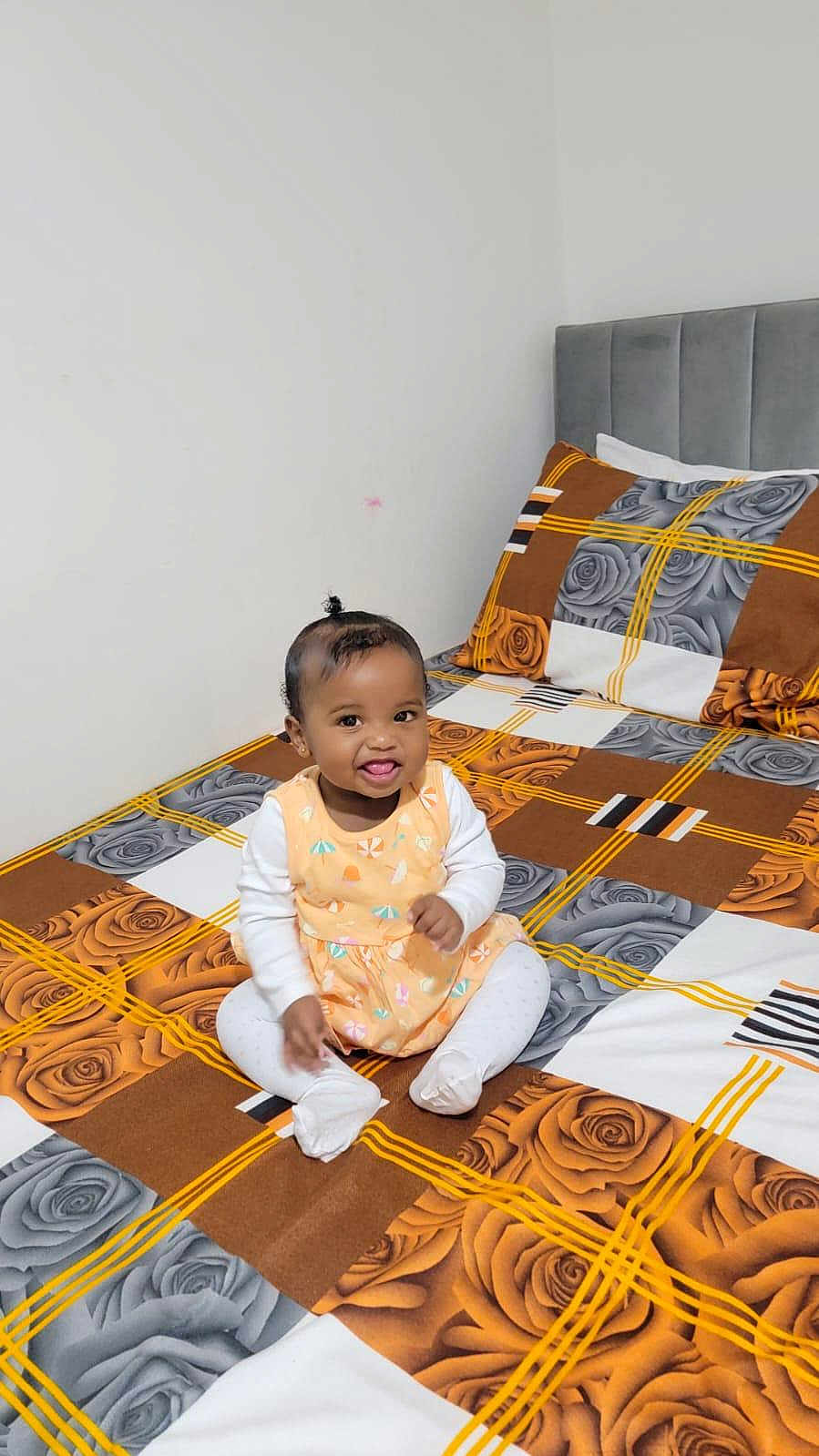Fatima joined the competition — help win amazing prizes! baby, child, smiling, sitting, bed, bedspread, plaid_pattern, floral_pattern, rose, indoors, cute, happy, person, clothing, white_socks, long_sleeves, head, hair, tongue_out, room