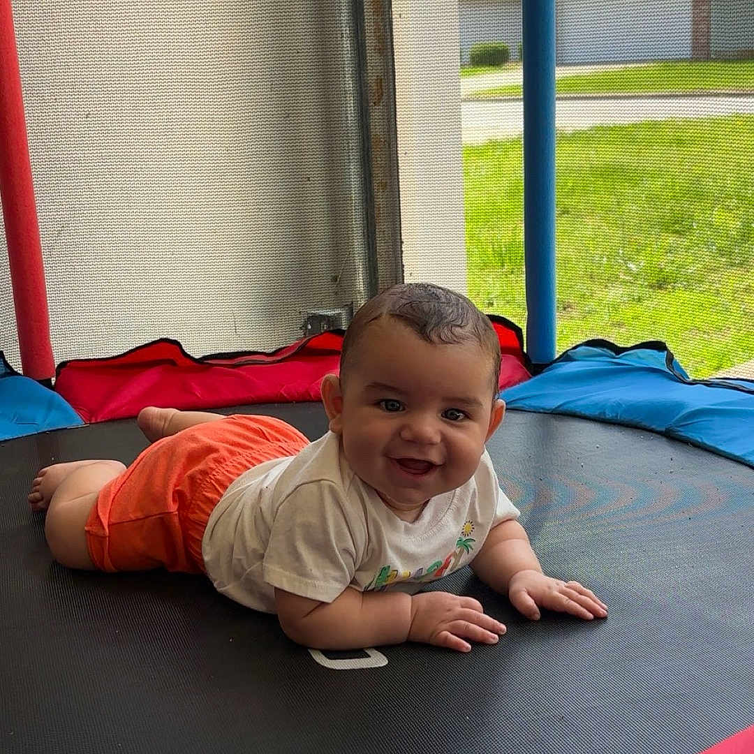 Branden joined the competition — help win amazing prizes! baby, backyard, child, colorful_padding, crawling, daylight, face, grass, happy, home, mesh_screen, orange_shorts, outdoor, person, playtime, smiling, sunny, toddler, trampoline, white_shirt