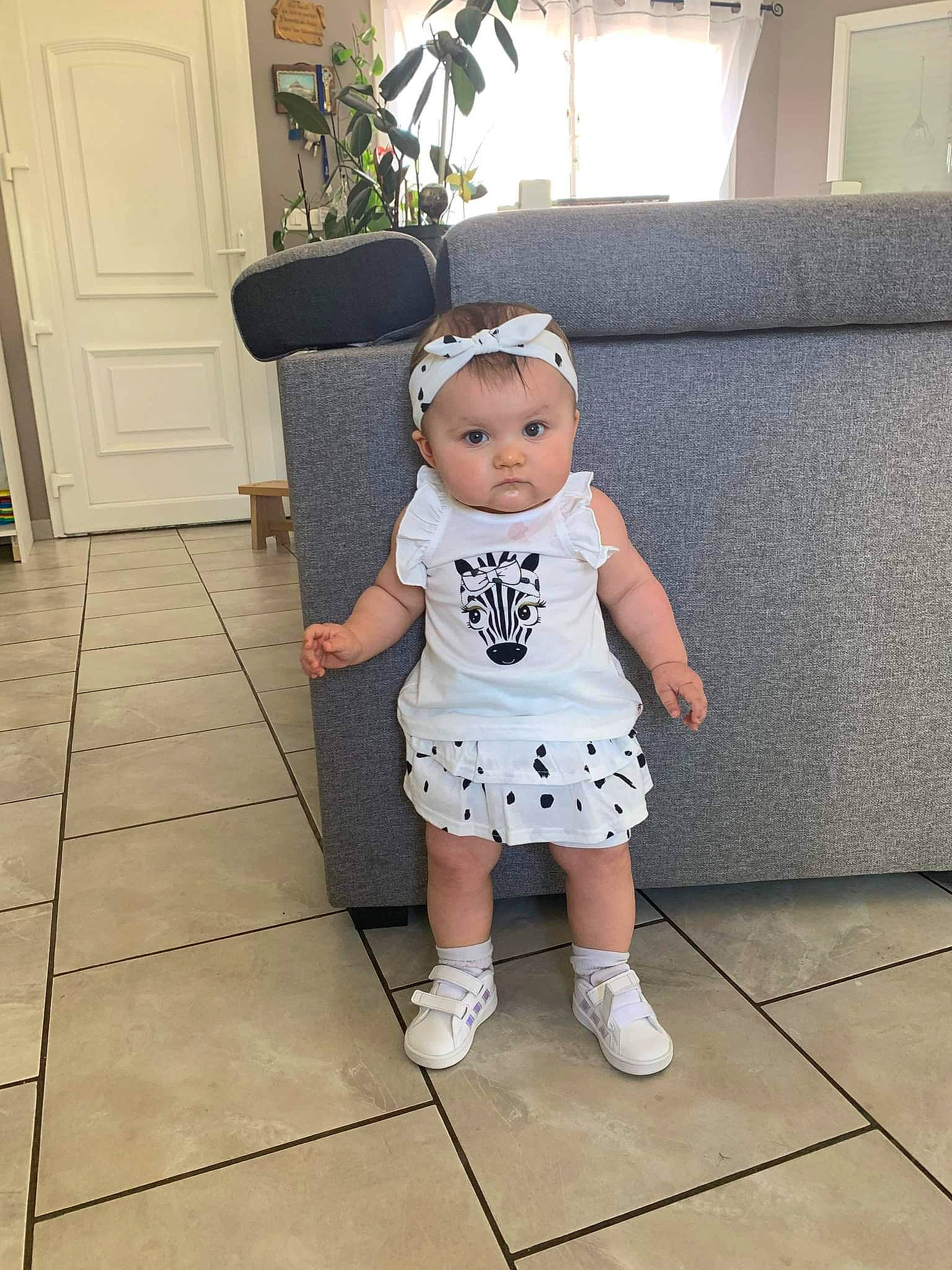 Maëlye participe au concours pour gagner de l'argent avec cette photo : baby, baby_toddler_clothing, clothing, door, floor, flooring, happy, hat, head, houseplant, human_leg, pattern, person, plant, shoe, shorts, sleeve, t_shirt, thigh, toddler