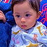 baby, child, onesie, animal_print, colorful, patterned_background, face, portrait, indoor, seated, attention, cute, young, person, clothing, technology, phone_screen, lock_screen, time_display, date_display