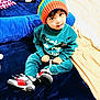 Moh is registered to the contest to win money with this photo: child, toddler, hat, knit_hat, colorful, sneakers, blue_blanket, clothing, indoor, smiling, cute, young_child, sitting, portrait, face, cozy, playful, person, toy, home