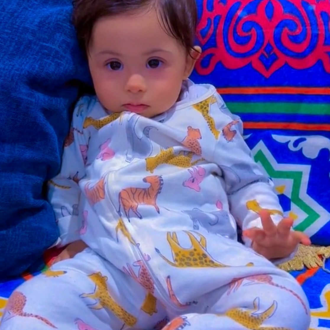 Moh is registered to the contest to win money with this photo: animal_print, baby, child, colorful_background, comfort, couch, cozy, cute, expression, face, hand, home, indoor, pajamas, patterned_clothing, portrait, relaxed, sitting, soft_furniture, young_child