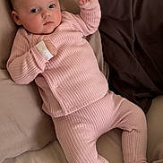 Nina participe au concours pour gagner de l'argent avec cette photo : baby, infant, pink_clothing, knitwear, bed, pillow, neutral_colors, person, child, cute, portrait, relaxing, indoors, soft_texture, sleepwear, young_child, resting, laying_down, small_hands, curious_expression