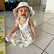 Naëlya a rejoint le concours — aidez-le/la à gagner de superbes lots ! baby, child, smiling, happy, dress, hat, floor, tile, indoor, person, cute, sitting, childhood, playmat, home, young, infant, apparel, headwear, joy