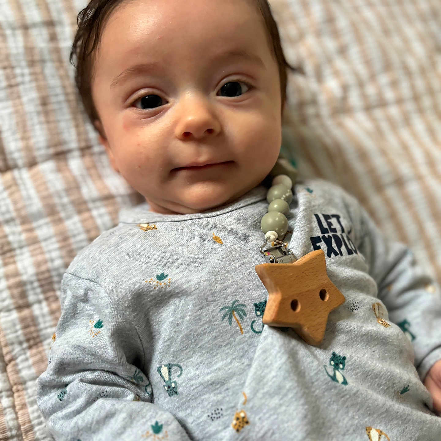 Julian a rejoint le concours — aidez-le/la à gagner de superbes lots ! animal_print, baby, beaded_clip, blanket, bokeh_background, close_up, cozy, curious_expression, eyes, face, hair, indoor, infant, lying_down, onesie, portrait, skin, soft_lighting, star_clip, wooden_star