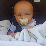 Kelsey is registered to the contest to win money with this photo: baby, pacifier, blanket, car_seat, child, infant, blue_eyes, face, head, clothing, person, sitting, closeup, cute, indoors, young_child, comfort, soft, wrapped, seatbelt