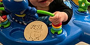 Shawn is registered to the contest to win money with this photo: baby, infant, child, orange_hat, activity_center, toy, blue, smiling, happy, face, indoor, floor, wooden_floor, play, colorful, hand, couch, furniture, person, closeup