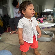 Santiago joined the competition — help win amazing prizes! baby_walker, barefoot, blurred_background, brown_shoes, candid, casual, child, concrete_floor, curly_hair, cute, outdoor, patio, person, porch, portrait, red_shorts, standing, toddler, toys, white_shirt
