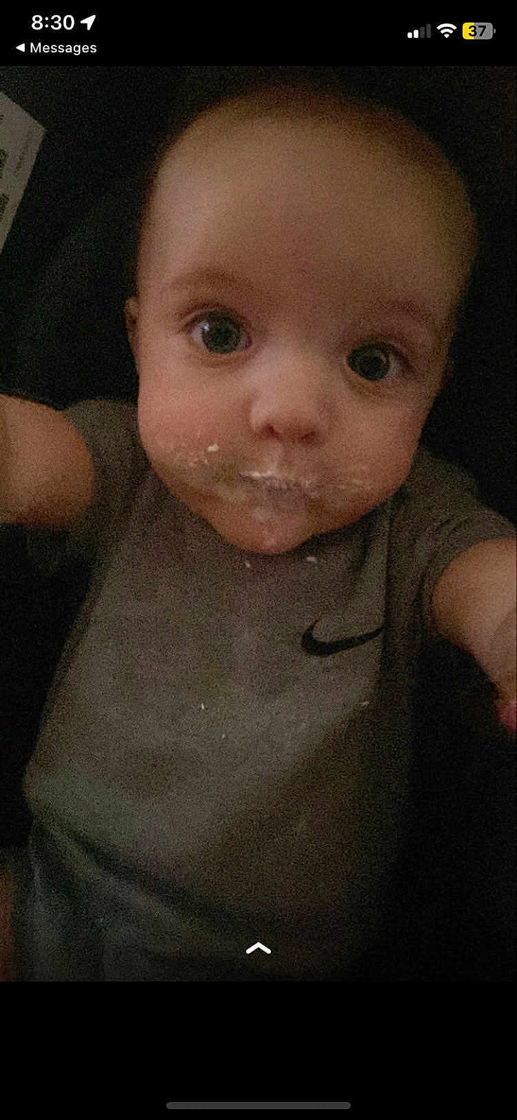 Neptune is registered to the contest to win money with this photo: baby, child, face, food, crumbs, shirt, grey_clothing, nike_logo, selfie, close_up, curious, wide_eyes, infant, young_child, messy_face, indoor, portrait, person, cute, expression