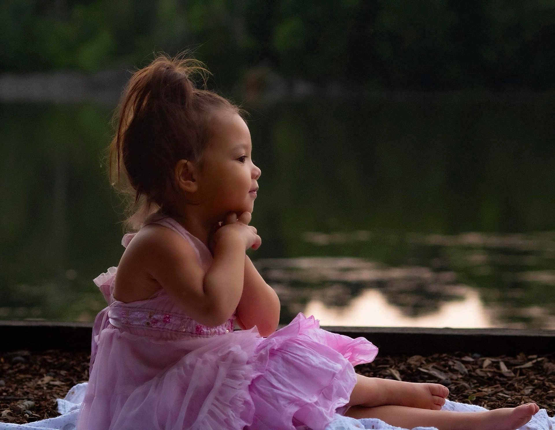 Kairi is registered to the contest to win money with this photo: child, girl, pink_dress, sitting, side_profile, water, lake, outdoor, nature, reflection, calm, evening, soft_light, young_child, barefoot, thoughtful, portrait, cute, peaceful, hair_up