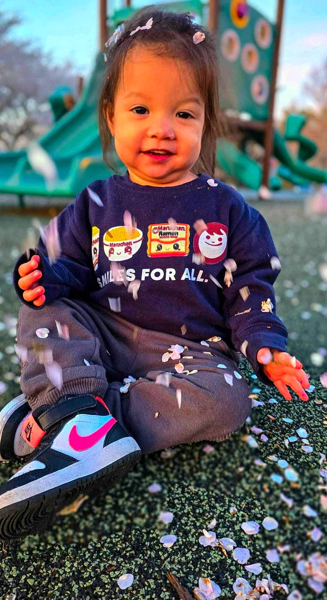 Kairi is registered to the contest to win money with this photo: bodypart, child, clothing, face, female, footwear, girl, grass, happy, head, outdoorplayarea, outdoors, pants, person, photography, plant, playarea, portrait, shoe, sitting