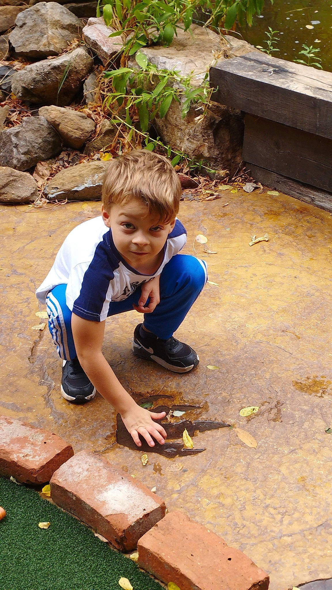 Aeden a rejoint le concours — aidez-le/la à gagner de superbes lots ! asphalt, boot, child, fish, flooring, fun, grass, landscape, leisure, person, plant, play, recreation, rock, shorts, sitting, smile, soil, t_shirt, toddler