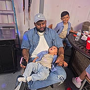 Jace is registered to the contest to win money with this photo: baby, baby_bottleless, baseball_cap, beard, child, children, colorful_lighting, denim, family, father, indoor, party, patio_furniture, playful, portrait, red_cups, sitting, smiling, string_lights, water_bottle