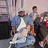 baby, baby_bottleless, baseball_cap, beard, child, children, colorful_lighting, denim, family, father, indoor, party, patio_furniture, playful, portrait, red_cups, sitting, smiling, string_lights, water_bottle