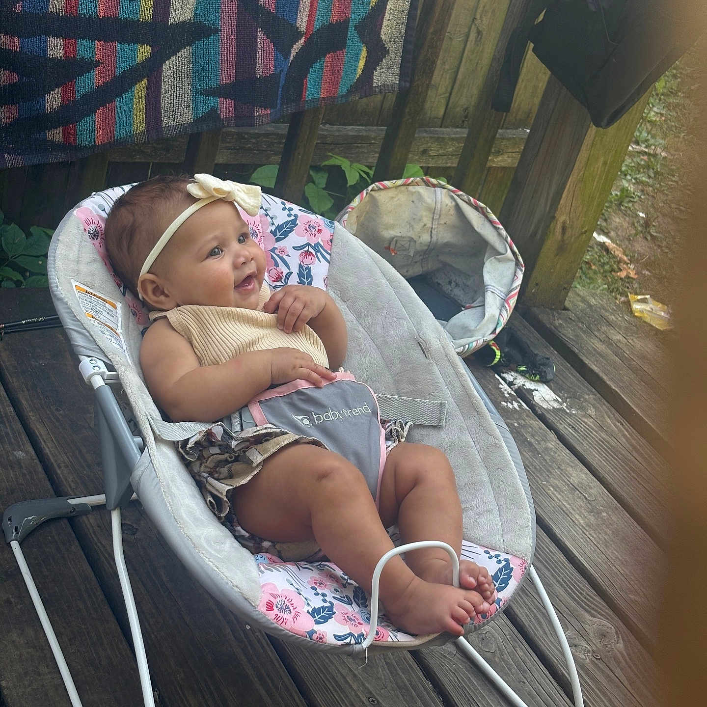 Kristiahnna joined the competition — help win amazing prizes! baby, baby_seat, blanket, bouncer, child, clothing, cute, fabric, flower_pattern, footwear, happy, headband, infant, outdoor, person, relaxing, skin, smile, toy, wooden_deck